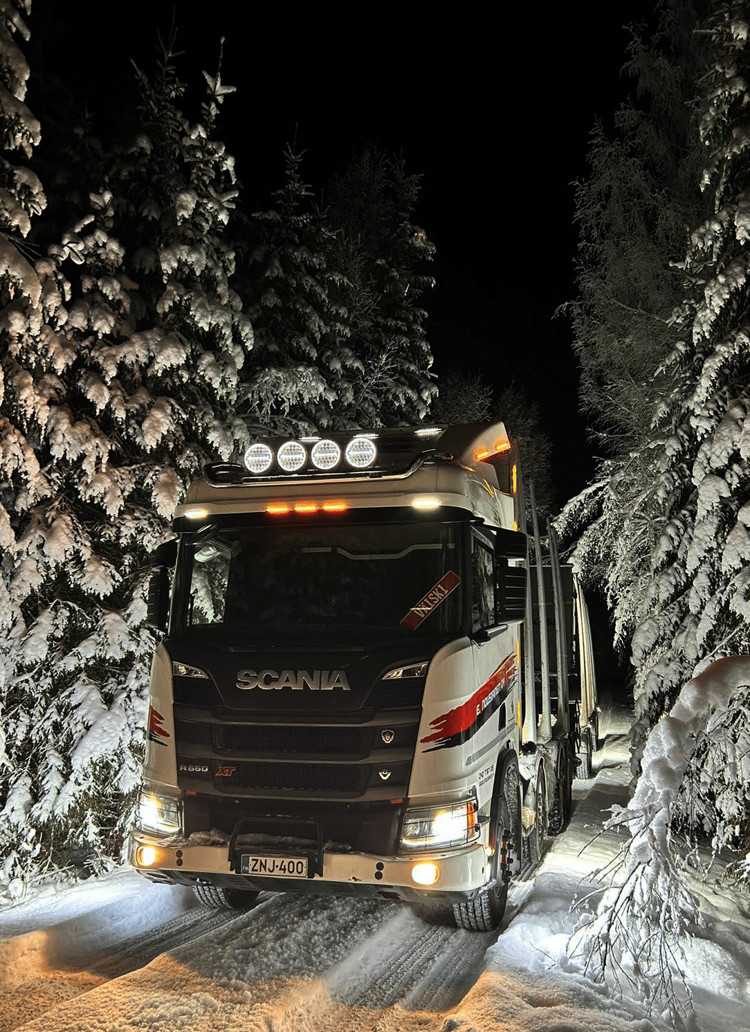 Kuljetusliike E. Nousiaisen puuauto taydessa lastissa talvisessa iltahamarassa metsatiella.